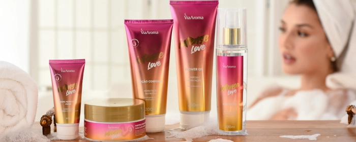 Mulher ao fundo tomando banho de banheira com uma tolha branca enrolado aos cabelos e a frente frascos de cosmeticos da Via Aroma da Linha Intense nas cores rosa e dourado.