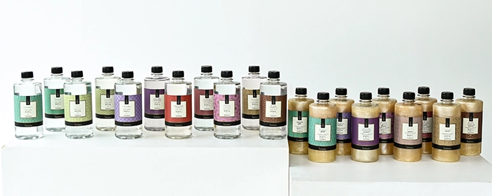 Em primeiro plano, há frascos de cosméticos da Via Aroma, com embalagens em tons marrom e dourado.