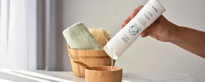 Mão de uma pessoa derramando um pote de shampoo da Via Aroma em uma vasilha de madeira