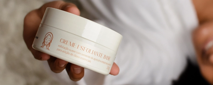 Mão de uma pessoa segurando um pote branco de esfoliante corporal da Via Aroma
