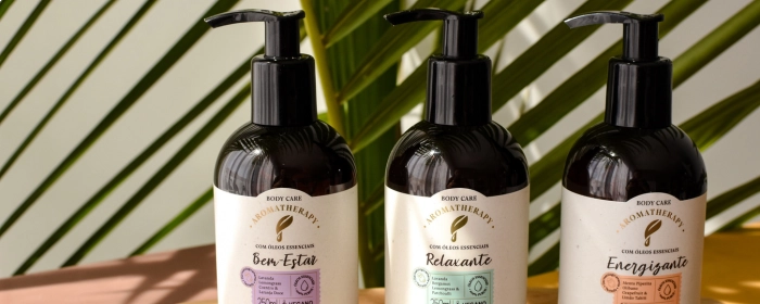 Três sabonetes em Líquido Via Aroma e um fundo com plantas sombreadas pelo sol