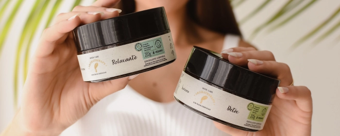 Mão de uma pessoa segurando dois potes de esfoliante da Via Aroma 