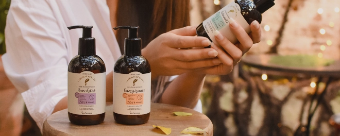 Mulher segurando um frasco de sabonete líquido Via Aroma com mas dois frascos na na frente da cor âmbar